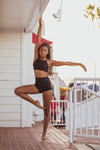 Model wearing Aura7 Activewear high waisted rigel shorts doing yoga pose on a balcony