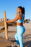 Model wearing Aura 7 Activewear Fresh Air Capella legging yoga pants climbing up a lifeguard tower on the beach