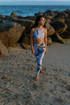 Model wearing Aura 7 Activewear Tropic Del Mar Top posing on the beach at sunset in front of rocks