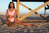 Model wearing Aura 7 Activewear Flower Rigel short doing a yoga pose on the beach in front of a lifeguard tower