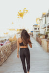 Model wearing Aura7 Activewear Vita legging yoga pants walking on a sunny sidewalk near the beach